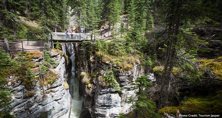 Two people lean over a bridge over the flowing water.