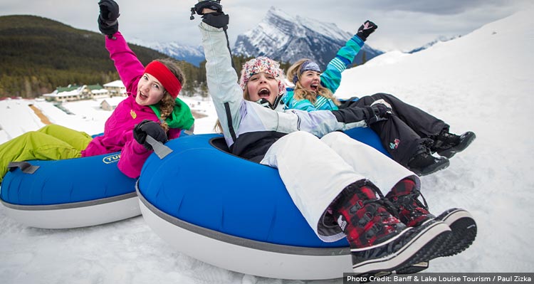 Three children tubing down a mountain side in the snow, mountain behind.