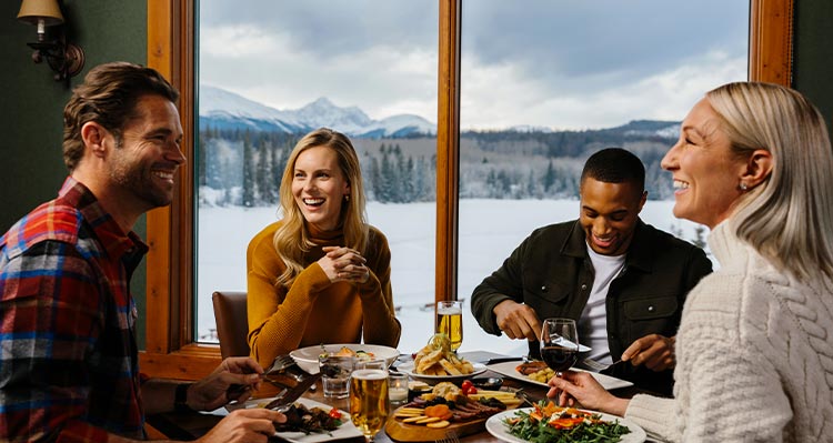 Four people enjoying a meal at a dining table, a window with winter scenery behind them.