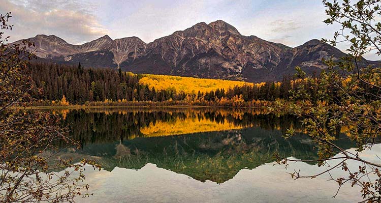 A lake in the fall, with orange trees and a mountain range in the background.