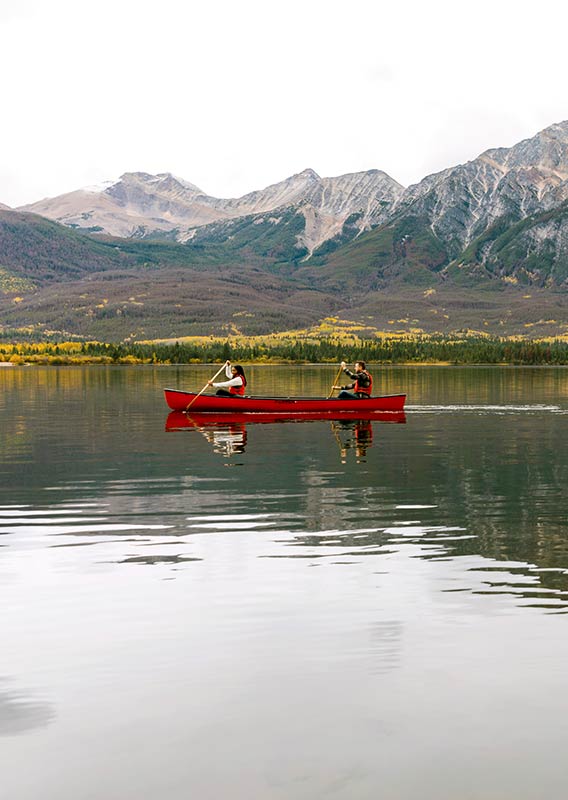 A clear lake in Jasper with two people rowing in a red canoe.