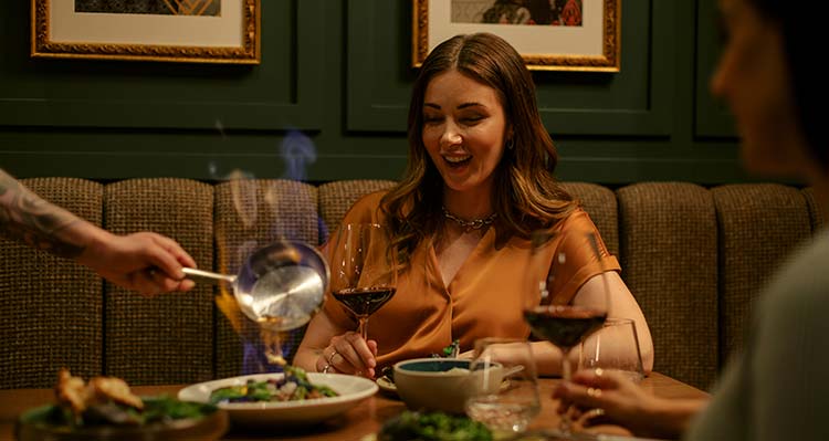 A woman sits at a table and a server plates her meal