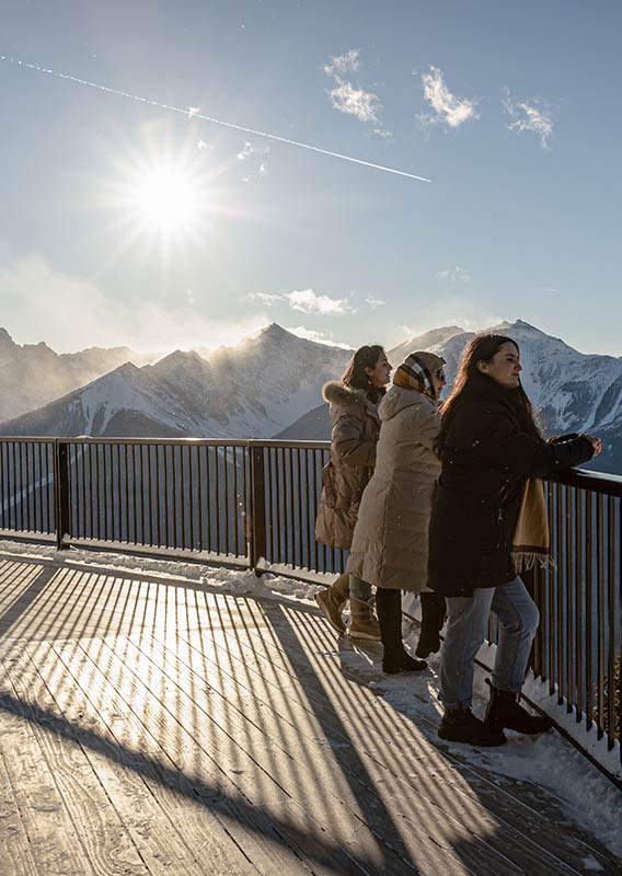 Three women stand on the balcony of the Banff Gondola in winter.