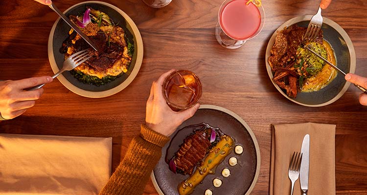 Above view of a table full of dinner plates and cups with hands reaching for items.