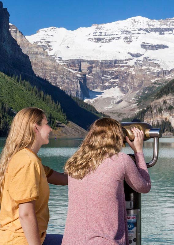 Two women look out at a lake surrounded by snow-covered mountains