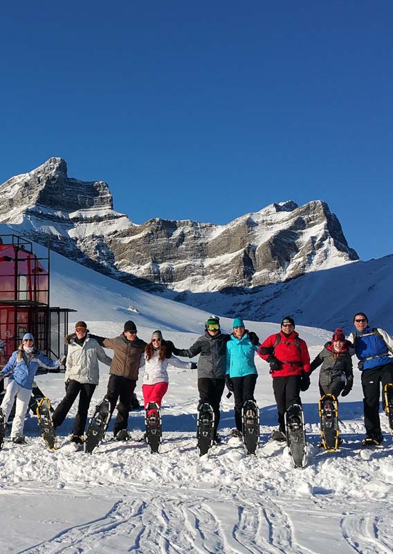 A group of snowshoers stand in a snowy landscape with a snowcat vehicle