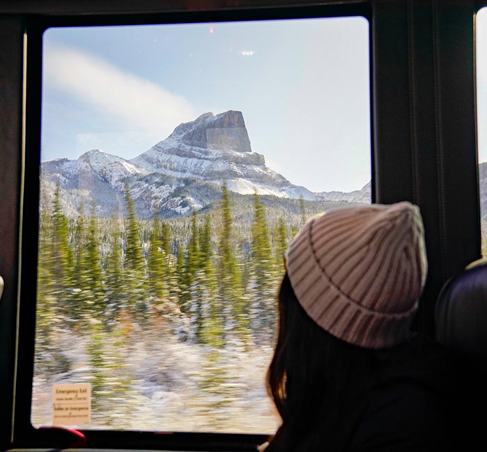 A person sits next to bus window, looking out at a tall mountain.