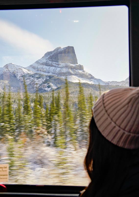 A person sits at a window seat on a bus, looking out to a mountain.