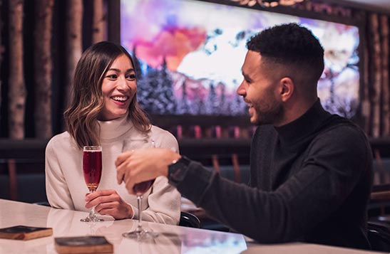 Two people sit at a restaurant bar with drinks.