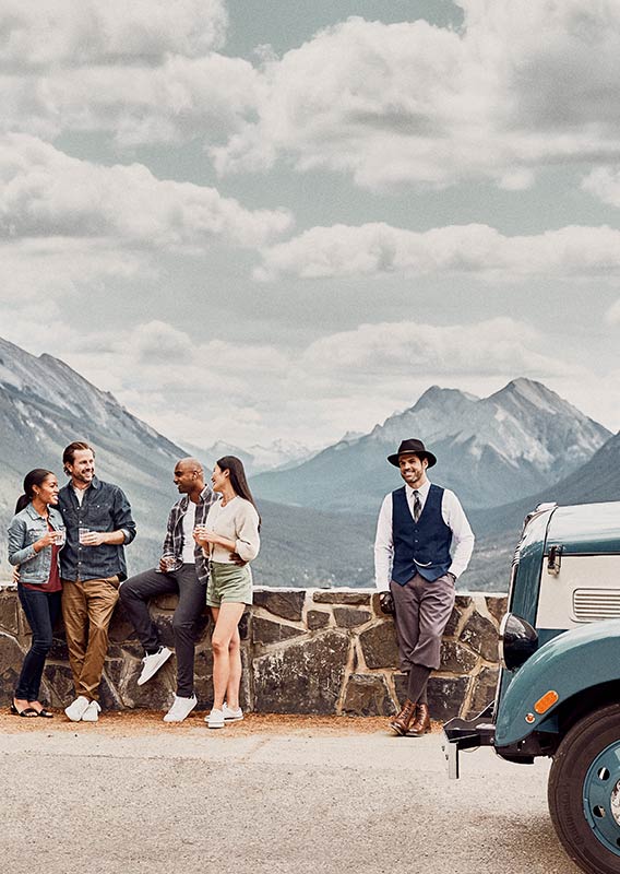 Guests and a tour guide stand outside with a historic vehicle parked next to them.