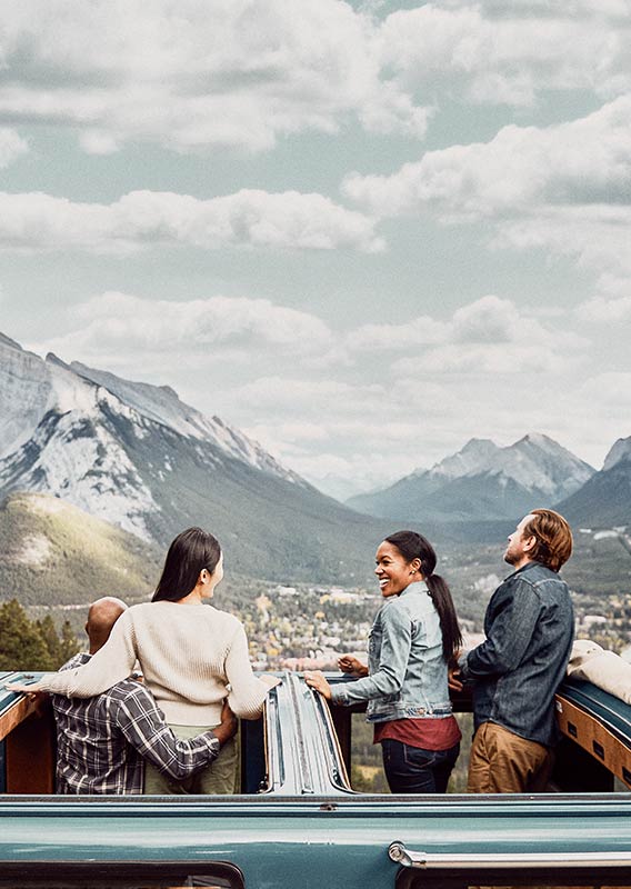 Guests stand through the roof of a historic vehicle and look down at the town of Banff.