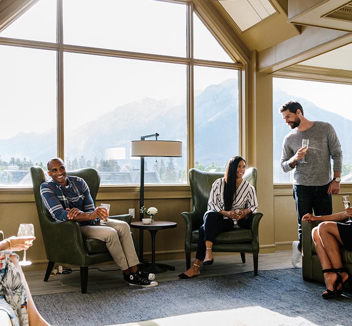 A group of people relax in a top floor lounge with large windows,.