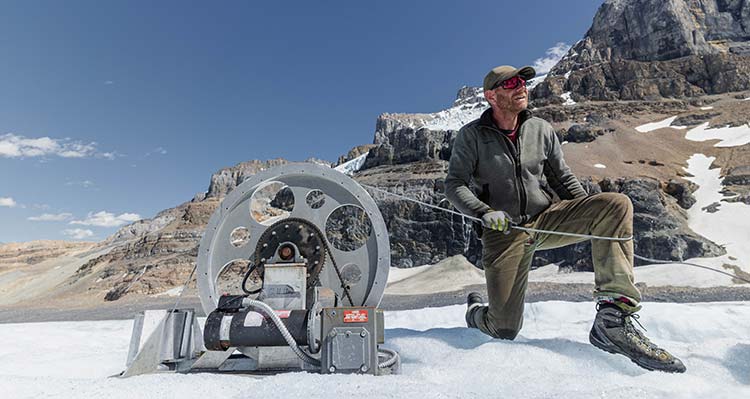 A researcher kneels on the Athabasca Glacier with tools