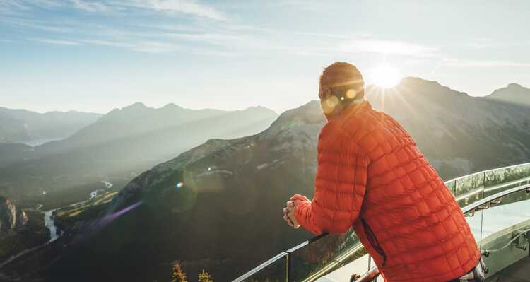 A person in a red jacket at a mountaintop viewpoint.