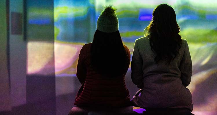 Two women sit inside a light display at Nightrise from behind.
