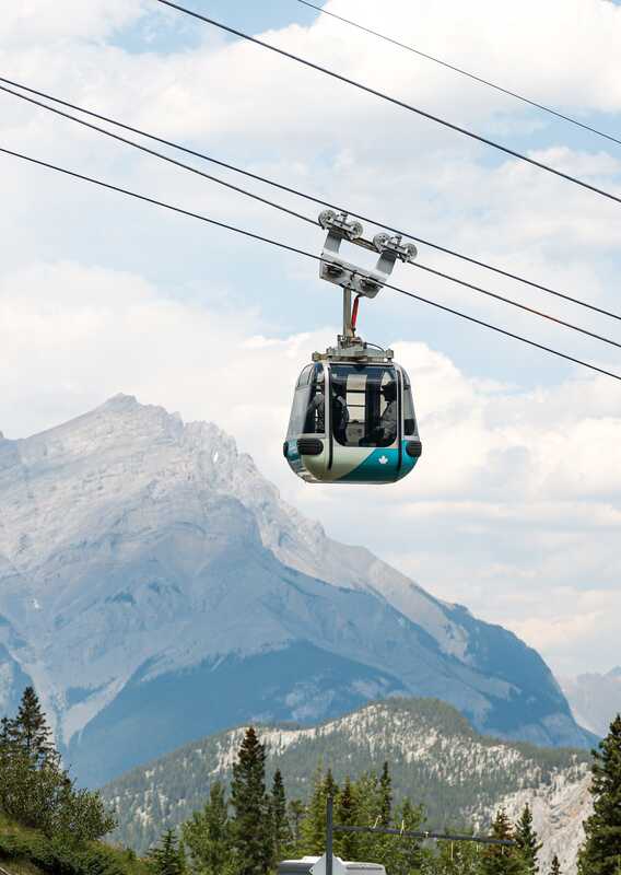 A Banff Gondola ascending the mountain in the spring, with mountain view in the background.