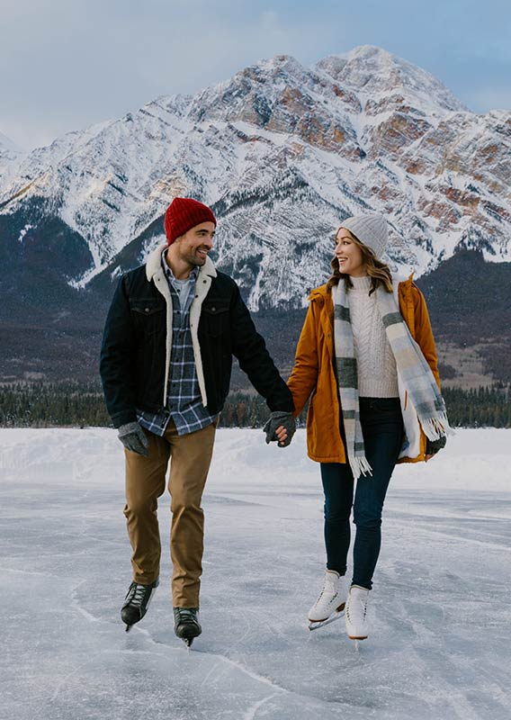 Two people holding hands ice skating on a frozen lake.