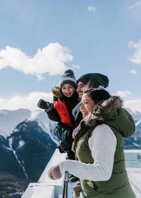 A young family of three stand at the Gondola lookout in winter.