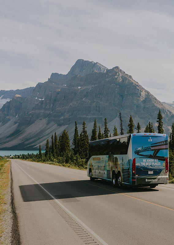 A bus drives down a road towards a lake and mountain.