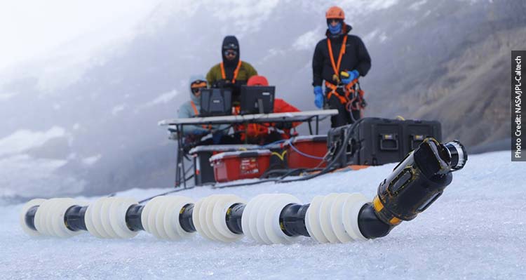Two researchers on the icefield look at the EEEL robot from a table.