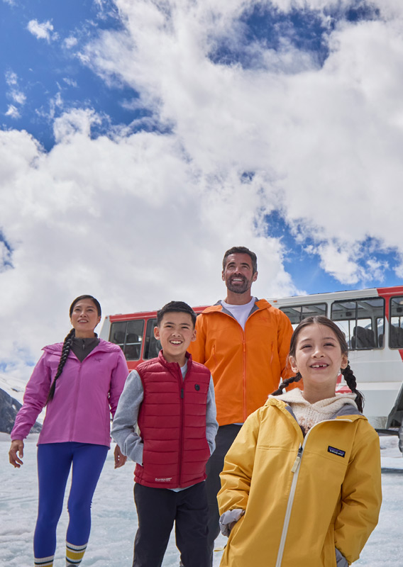 A family walking across Athabasca Glacier with an Ice Explorer Vehicle in the background.