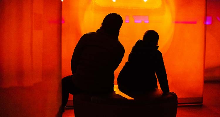 A parent and child sit inside Nightrise and look at a yellow and orange light display.