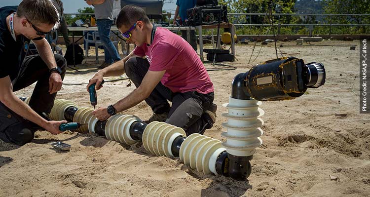Two technicians work on the EEL robot in the summer on the sand.