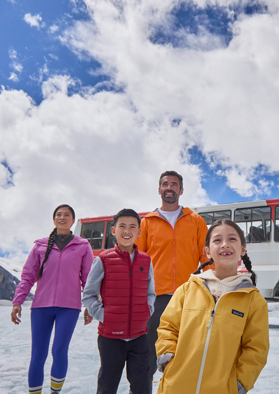 A family walking along the Athabasca Glacier, with an Ice Explorer vehical in the background.