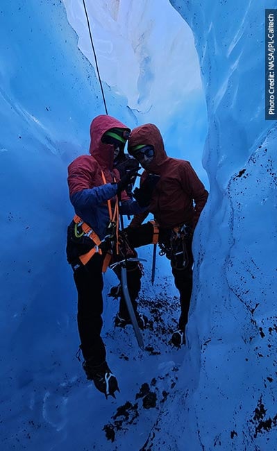 Two researchers on harnesses stand in an icy crevasse.