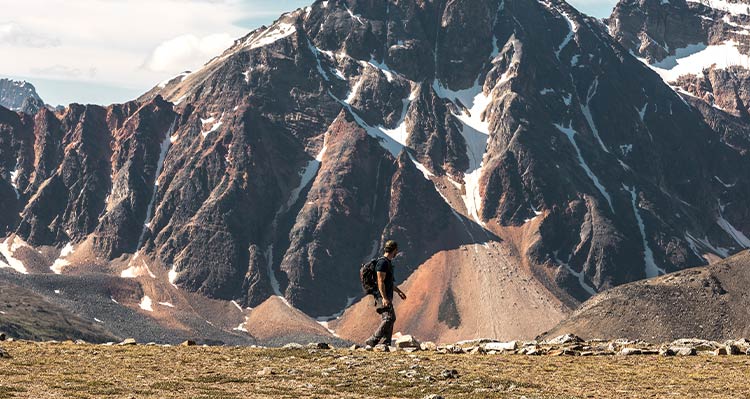 A hiker on an alpine path with tall mountains behind.