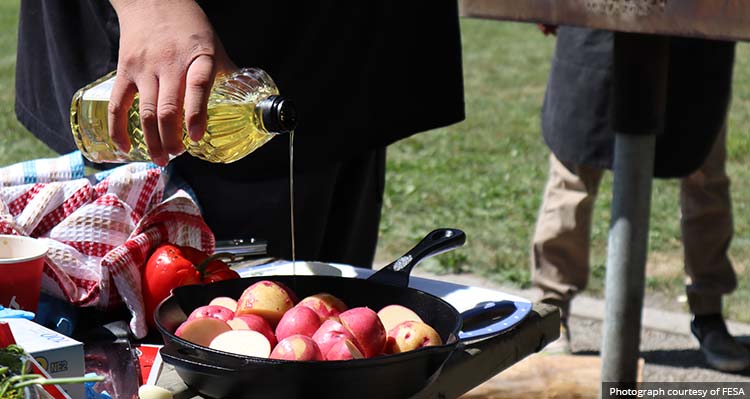 A person pours oil into a cast iron pan with apples in it.