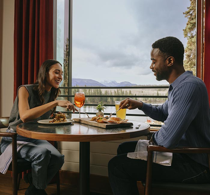 People sitting at dining tables near a large window overlooking a lake.