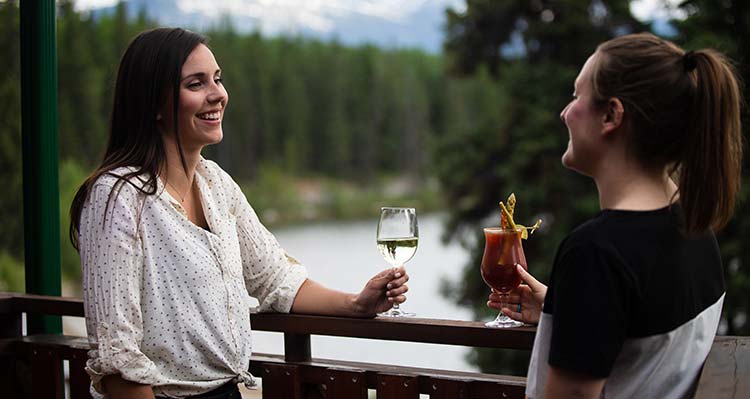 Two women have drinks on an outdoor patio with a mountain in the background.