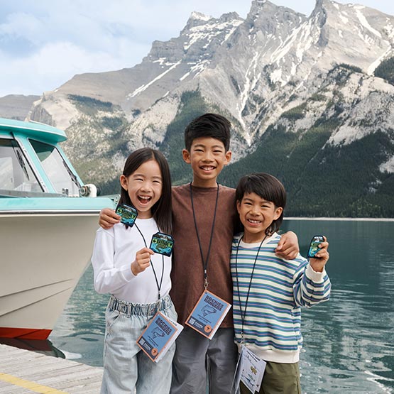 Three kids hold badges on a dock at a mountain lake.