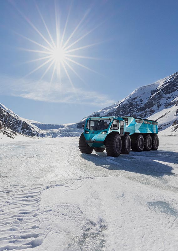 An all terrain Sherp vehicle parked on a glacier between tall mountains.