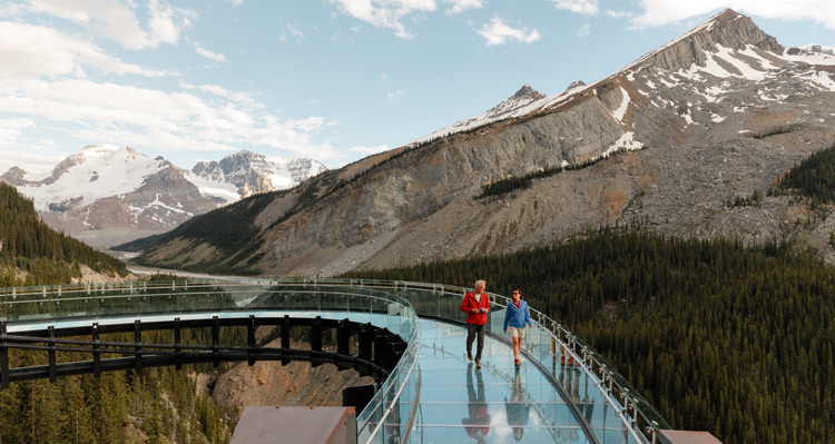 Two people walking along the Columbia Icefield Skywalk, looking at the mountain view.