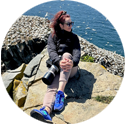 Author, Jenn Smith Nelson sitting on a rock beside the water.