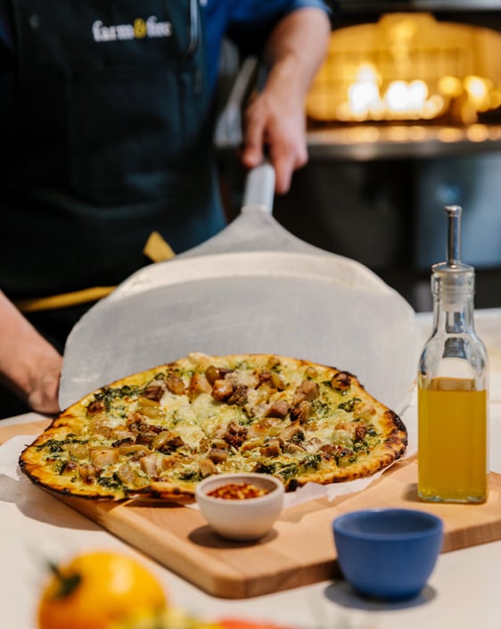 A cook plating a pizza at Farm and Fire
