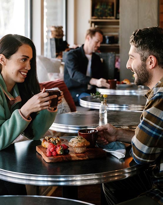 Two people sit at a small table with coffees and pastries.