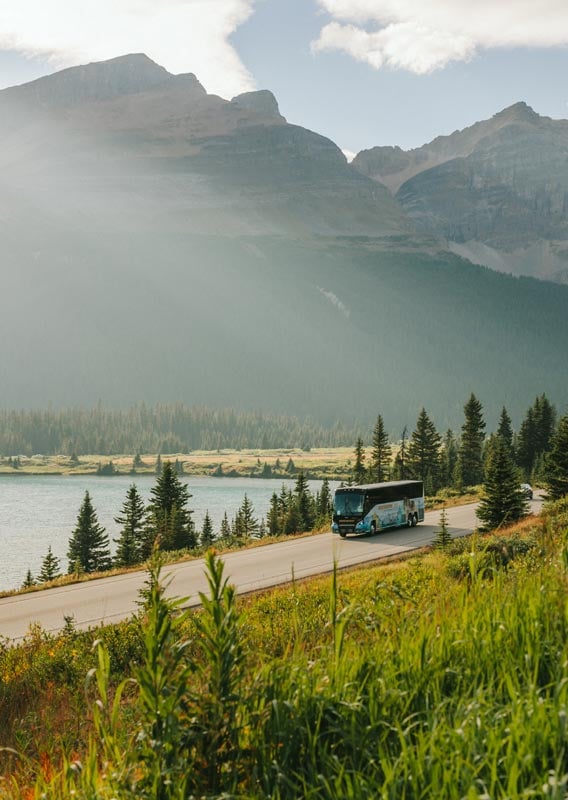 Brewster bus driving along a road between a hillside and a lake.