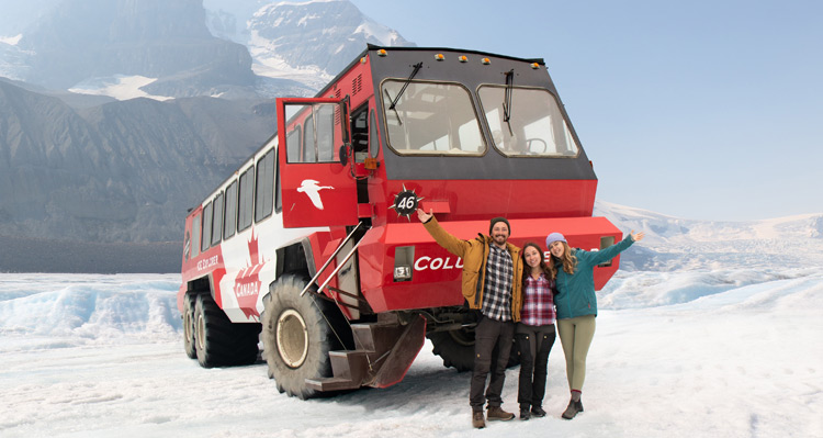Three people standing in front of an Ice Explorer vehicle, with a mountain view in the background.