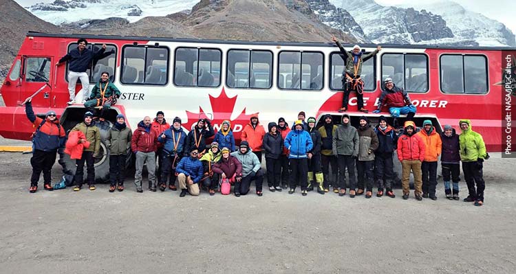 A large team of researchers pose in front of a Columbia Icefield Explorer vehicle.