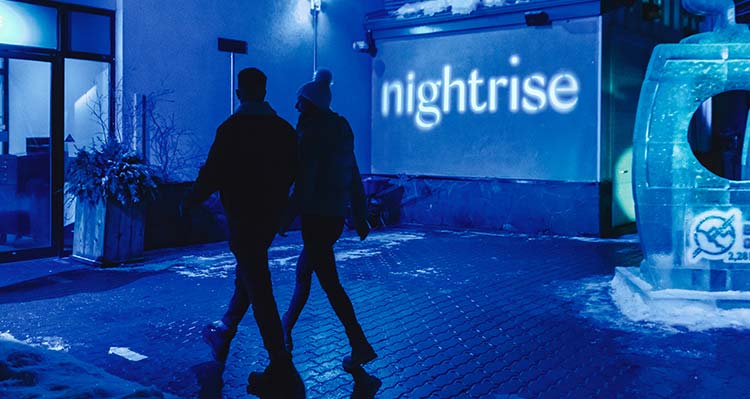 A couple walk into Nightrise at night, illuminated with blue light.