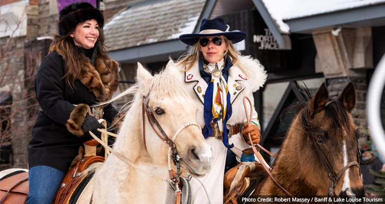 Two people riding horses along Banff Avenue