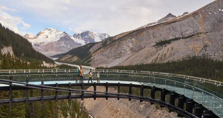 A family walking along the Columbia Icefield Skywalk, with mountains in the background.