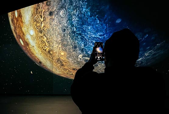 A person takes a picture of a planet exhibit in a dark room.