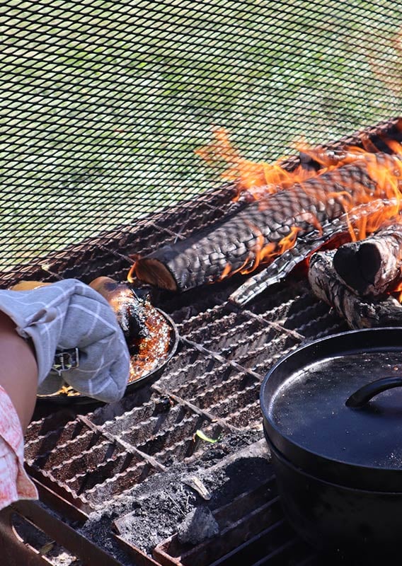 A person cooks a fish on an open fire outdoors.