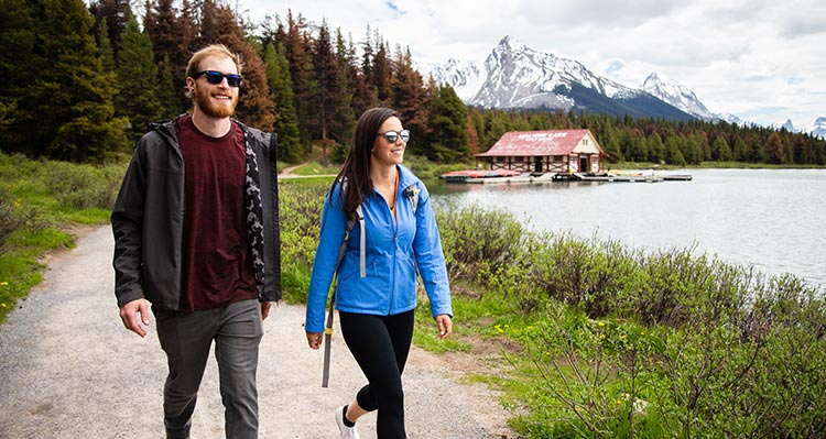 Two people walking on a lakeshore trail by the forest.