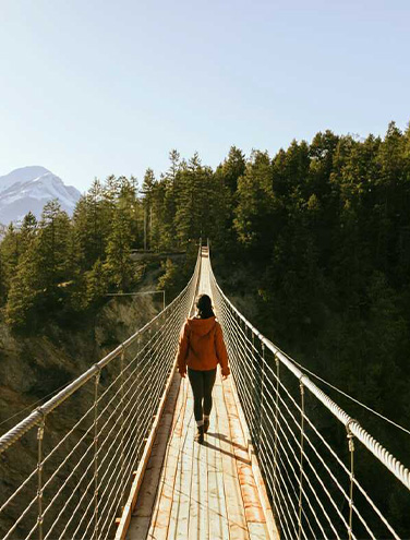 A person walks down a wooden suspension bridge over a canyon.