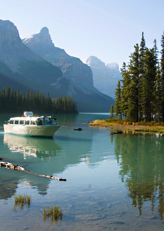 A boat approaches the shore of a lake surrounded by mountains.